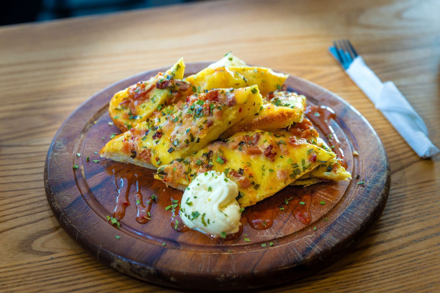 Artisanal flatbread with fresh herbs and dollop of cream served on rustic wooden board.