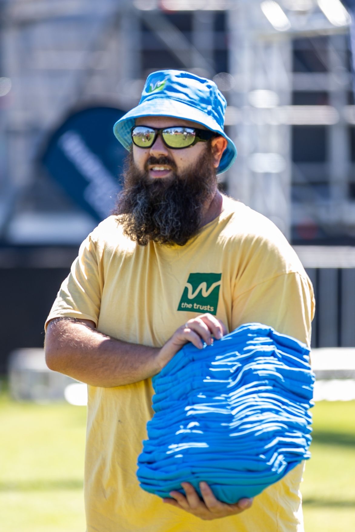 Staff member in yellow shirt holding blue promotional materials outdoors.