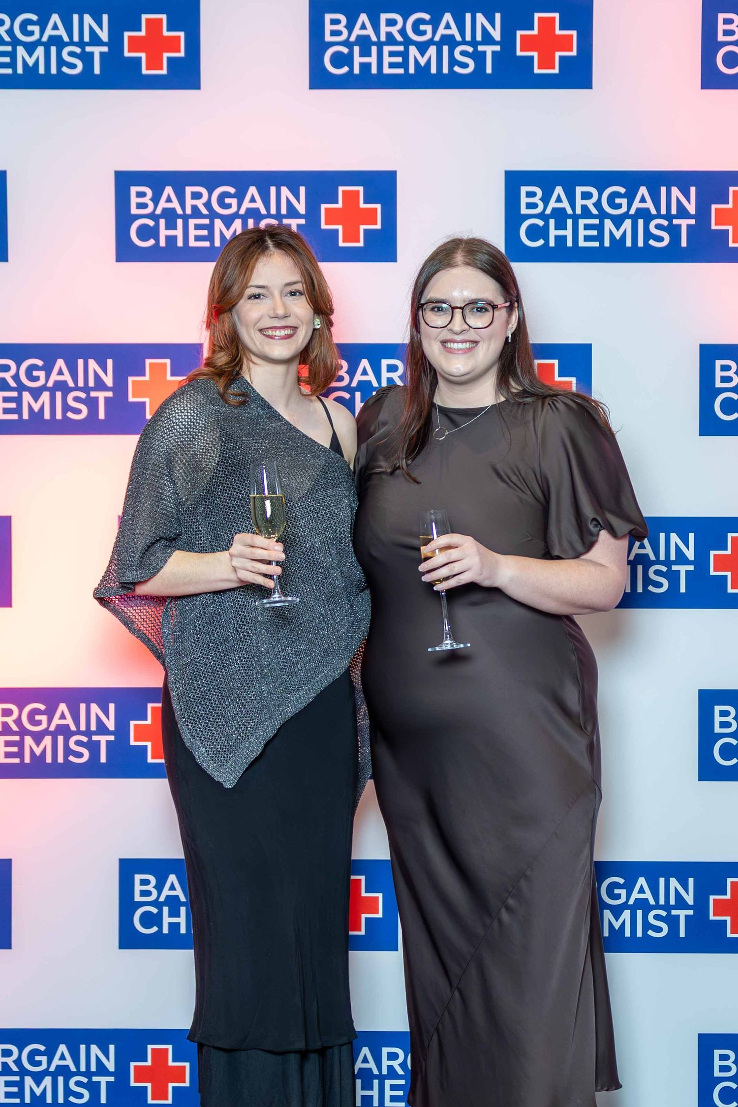 Group photo against Bargain Chemist branded backdrop at corporate event.