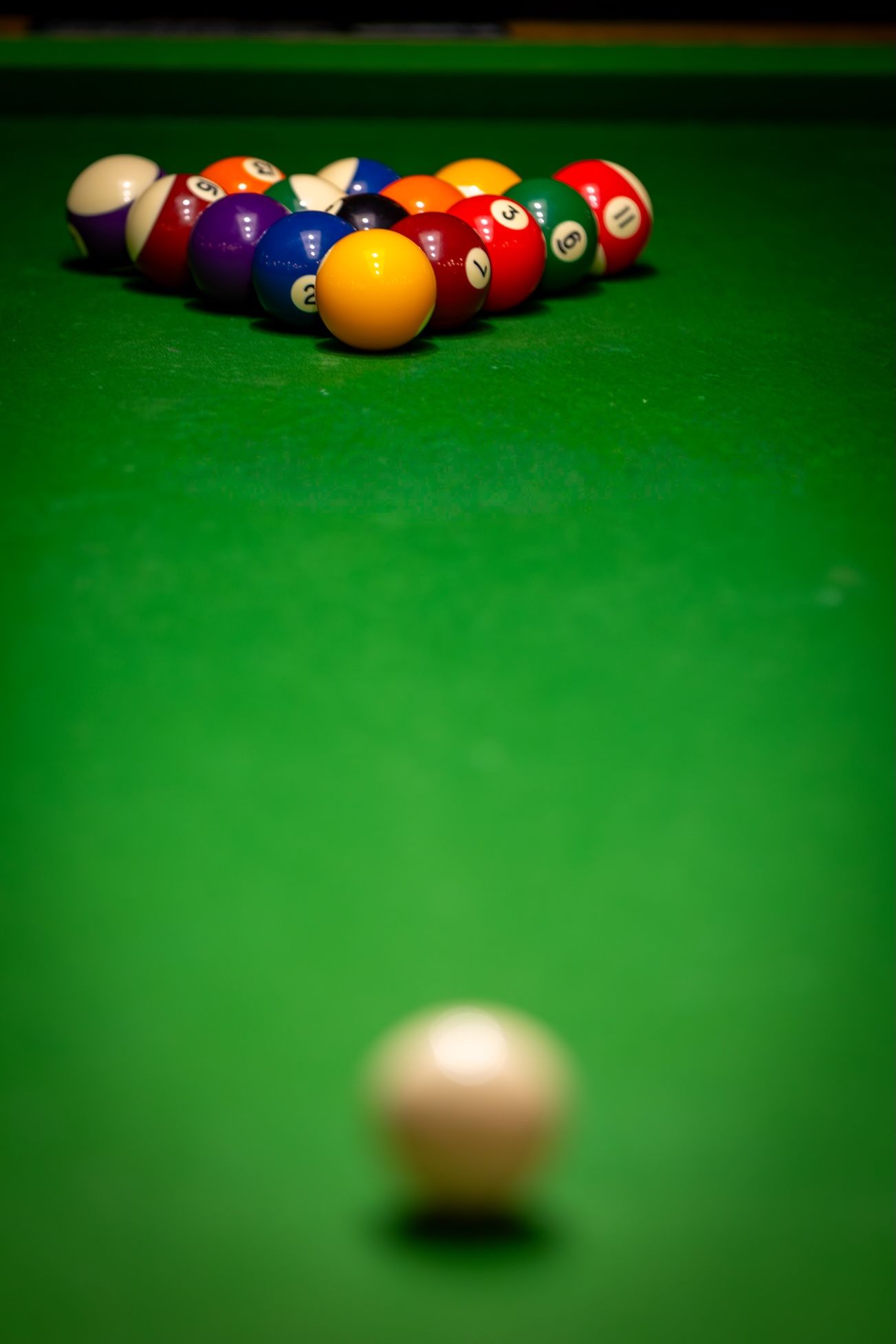 Pool balls racked on a green felt table with white cue ball in foreground ready for break shot.