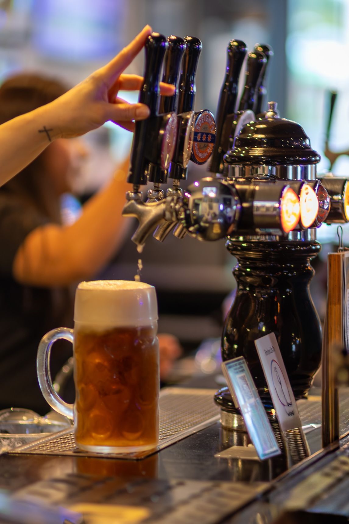 Draft beer being poured from tap into glass mug at bar counter with foam head forming.