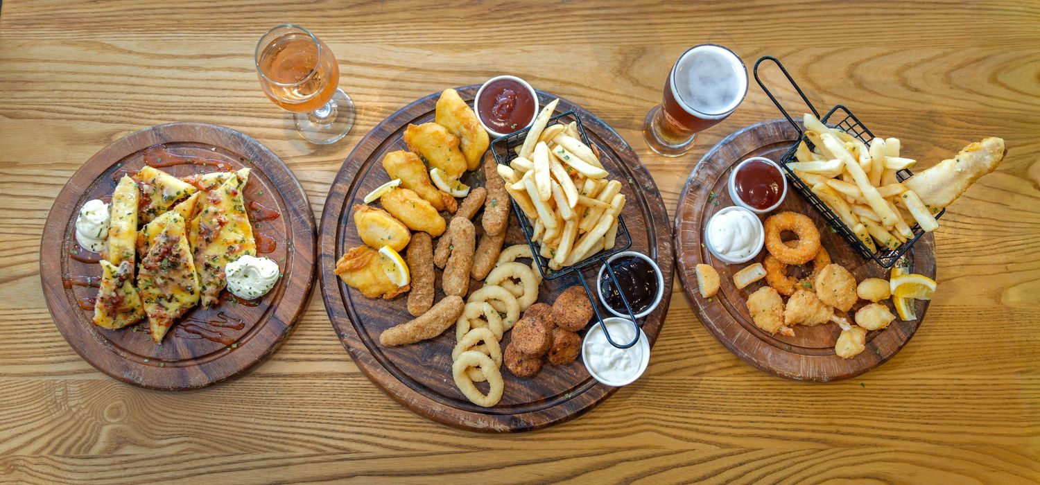 Panoramic view of wooden table with various pub appetizers and beer glasses arranged neatly.