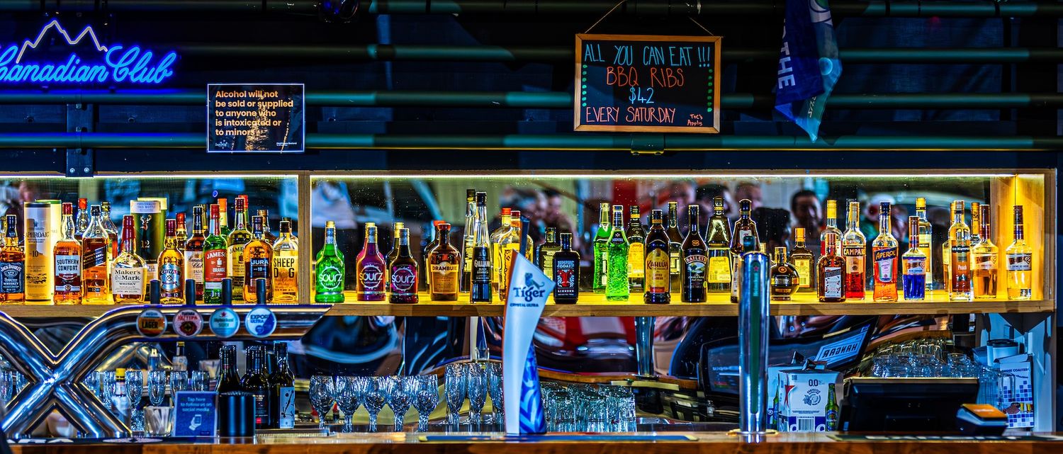 Neon-lit bar interior with glowing blue lights illuminating bottles and glasses on display shelves.