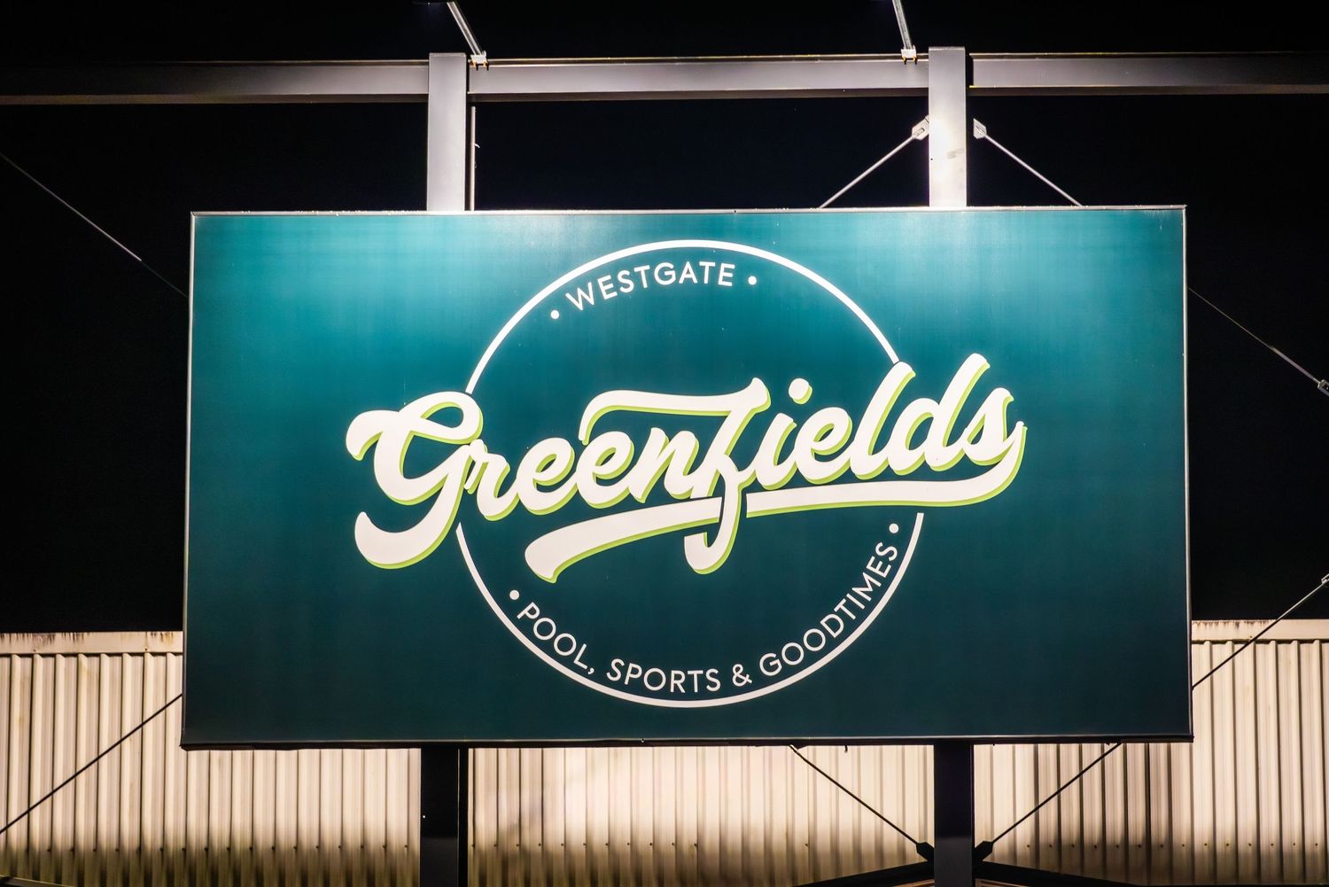 A large illuminated green sign displaying the Greenfields logo with white lettering against a dark background.