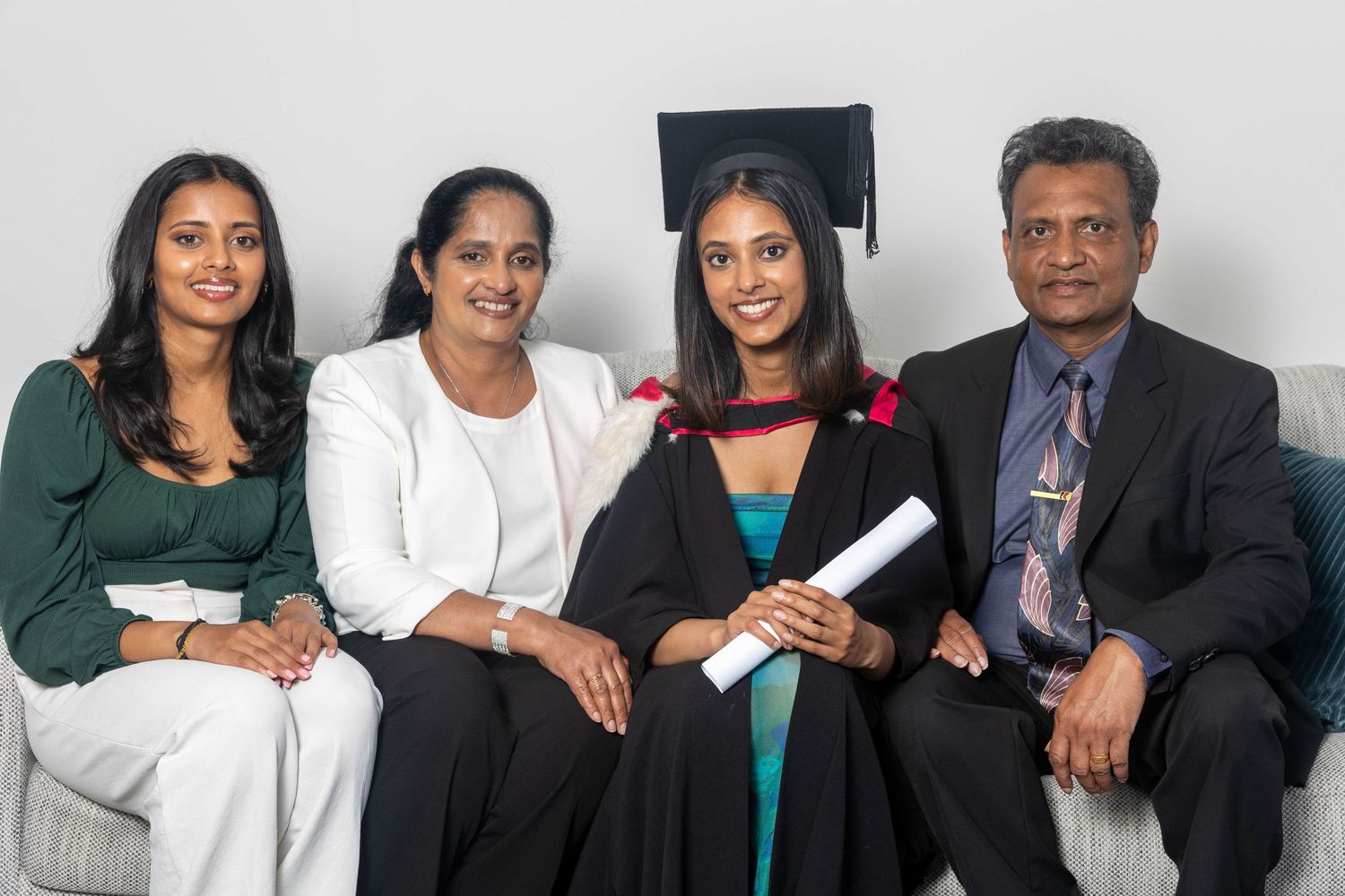 Family of four posing together at a graduation ceremony, with graduate wearing cap and gown holding diploma.