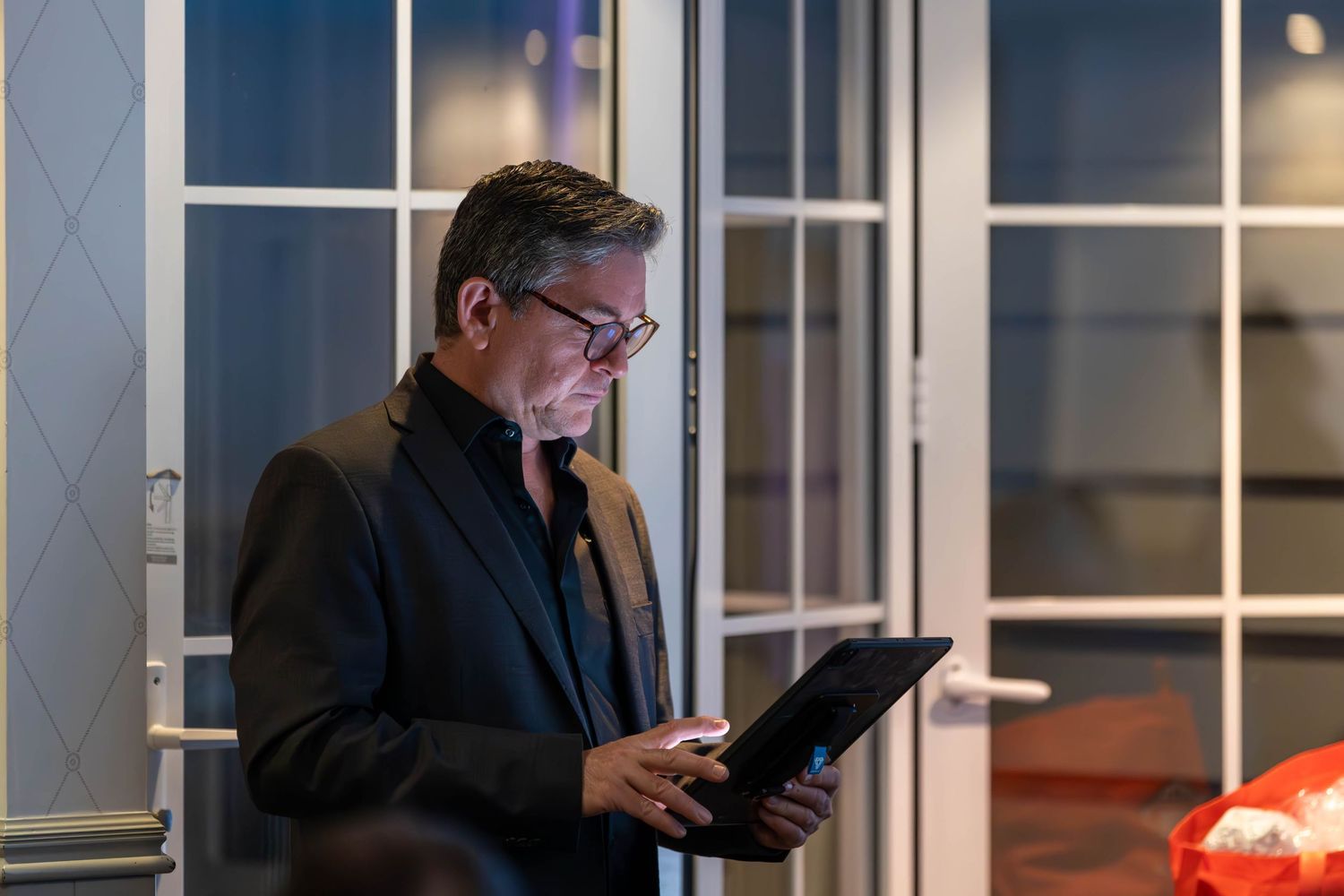 Professional man in glasses reviewing documents on a tablet in a modern office lobby at night.