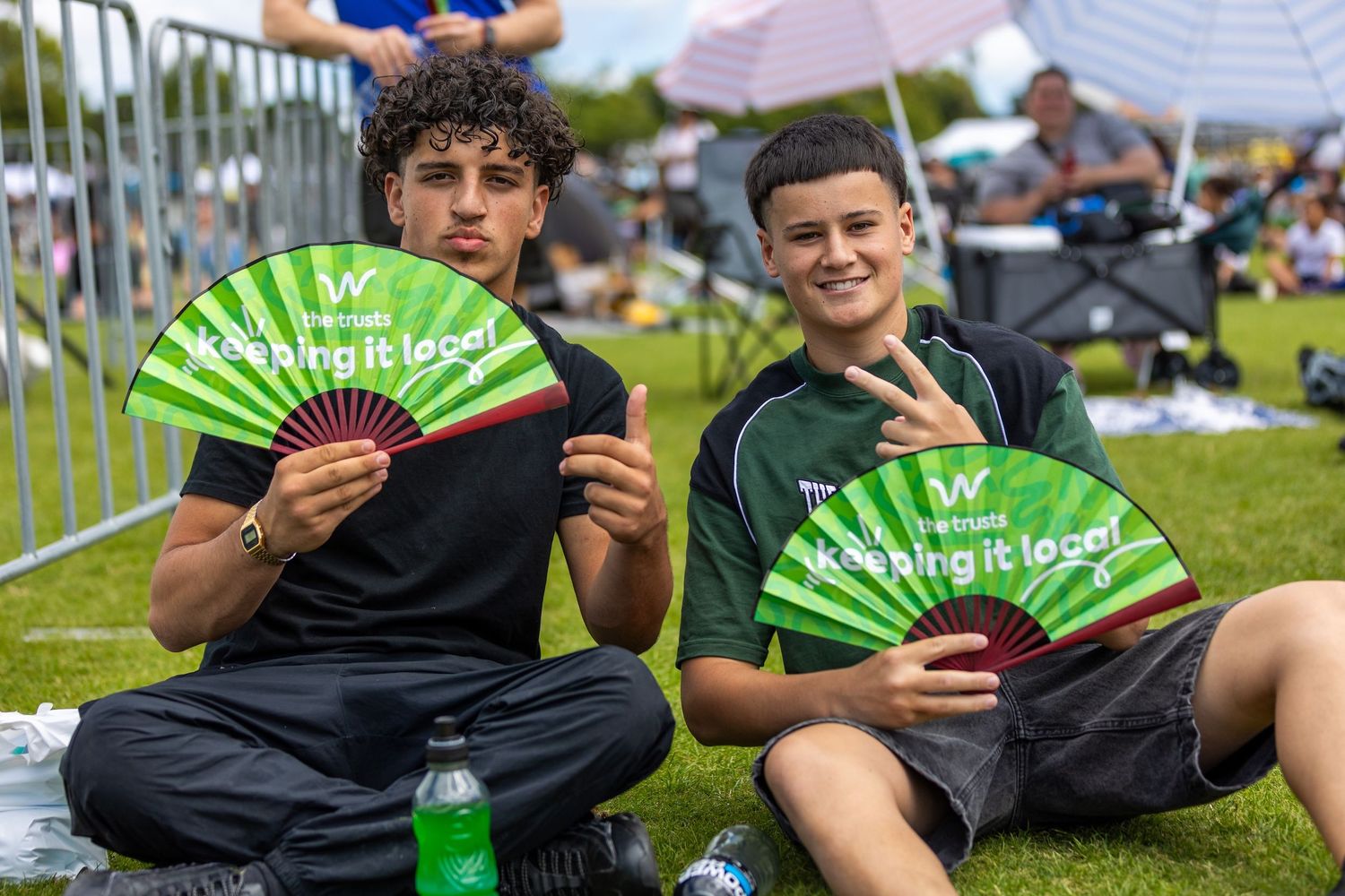 Group relaxing on grass with green promotional fans at summer festival.