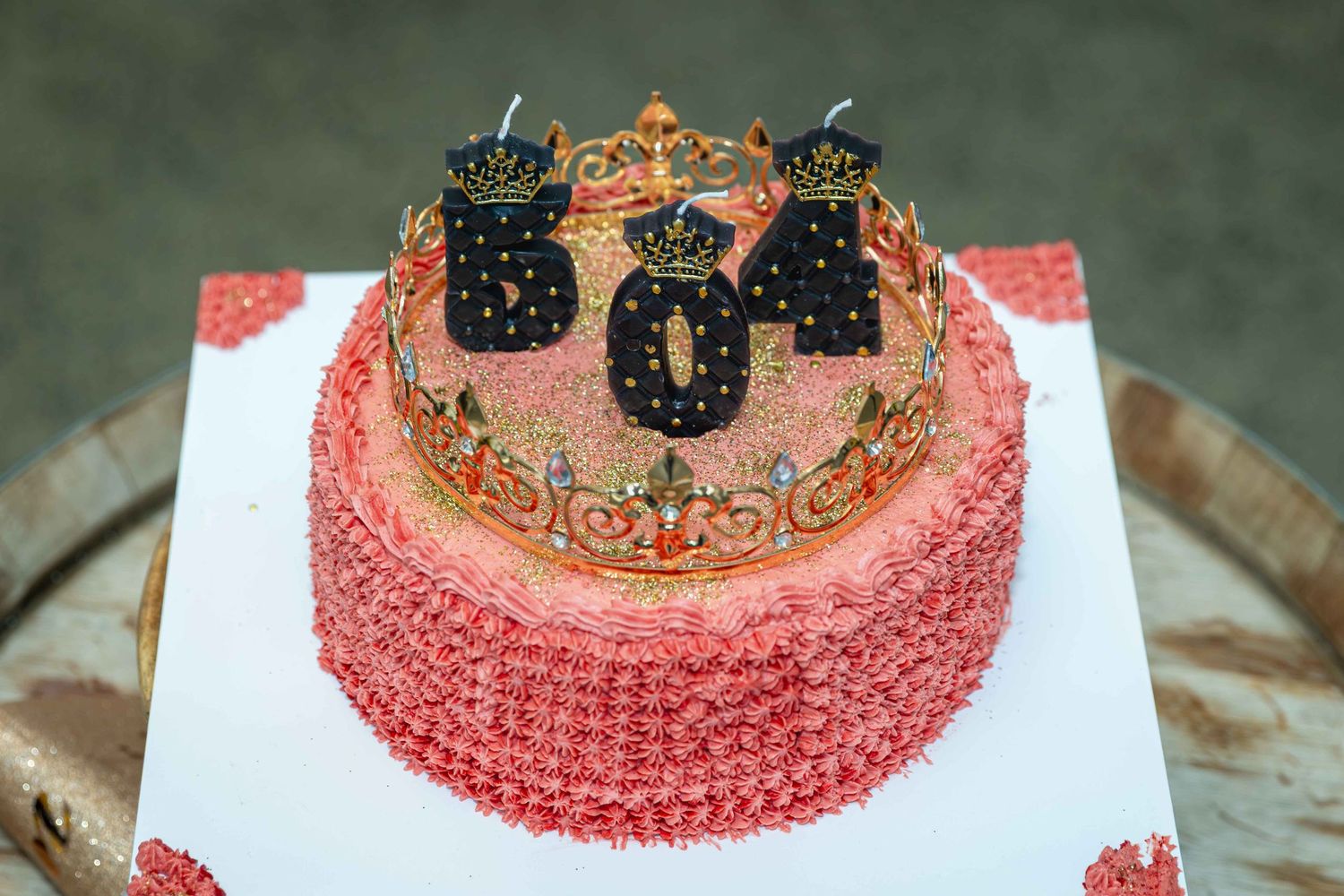 Pink birthday cake with crown decoration and number 504 candles on a white cake board.