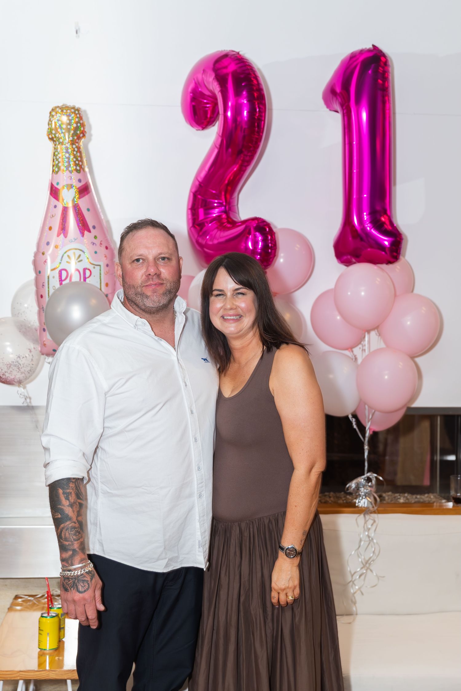 Couple posing at a 21st birthday party with pink balloons and champagne bottle balloon decorations.