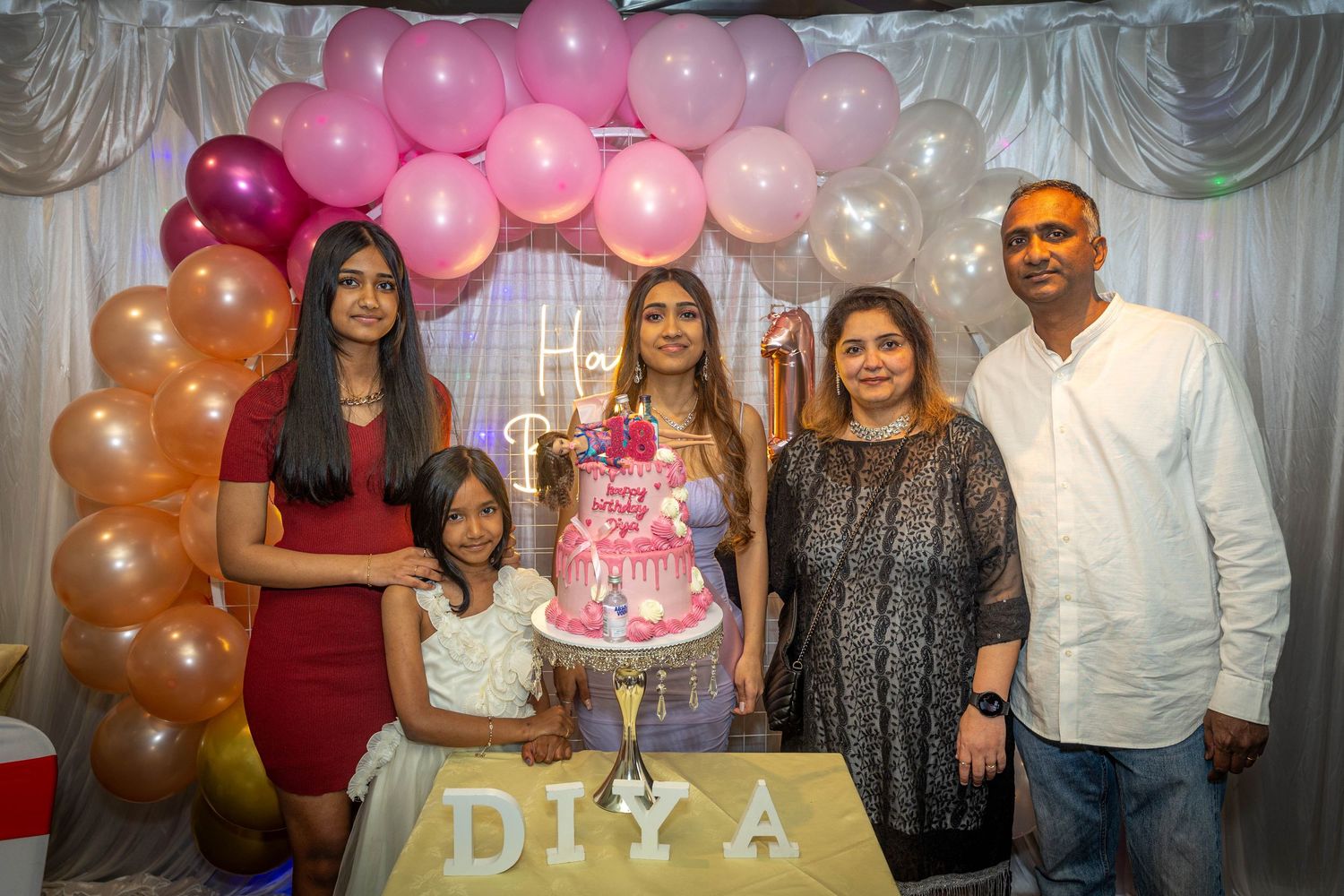 Family of five celebrating Diya's birthday party with pink balloons, decorations, and a decorated cake.
