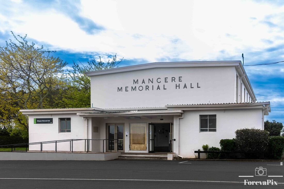 Mangere Memorial Hall exterior, a white building with signage, green trees, and a clear blue sky in Auckland, New Zealand.