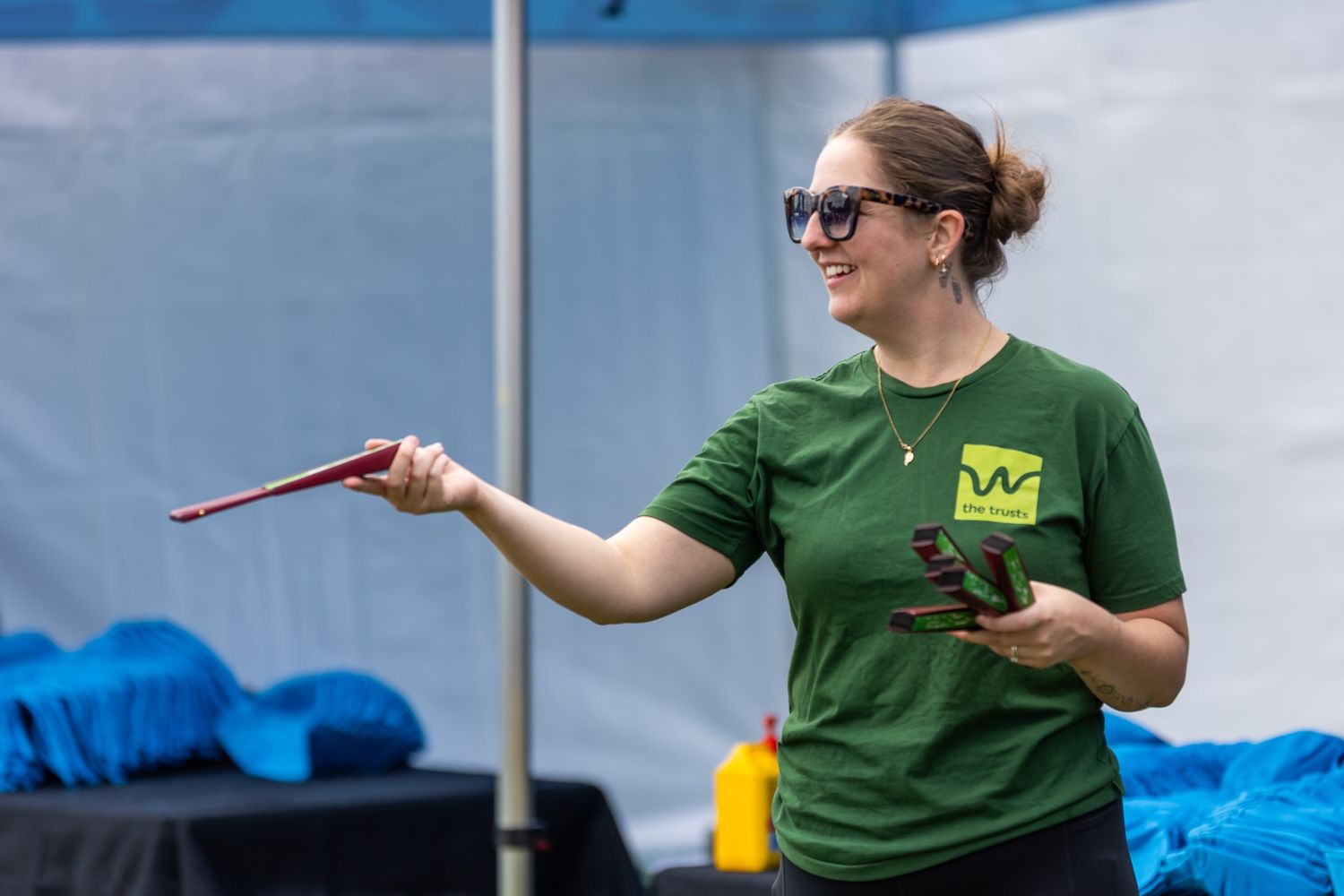 Event staff in green shirts working at outdoor booth with blue tent.