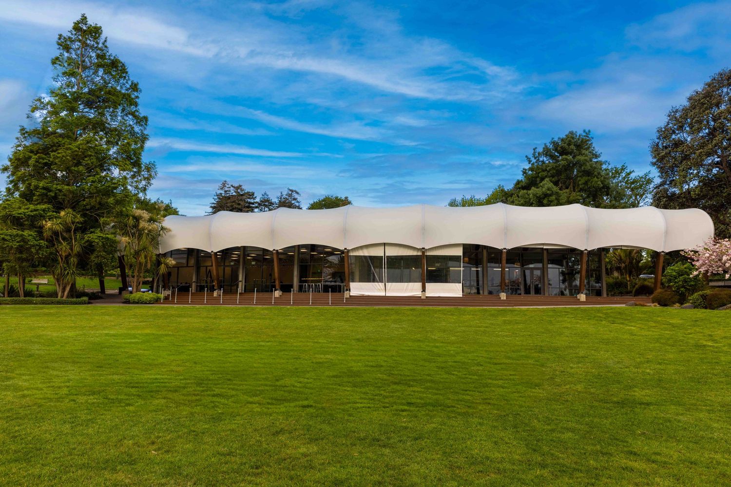 Panoramic view of a green lawn with white event tents and trees under bright blue sky.