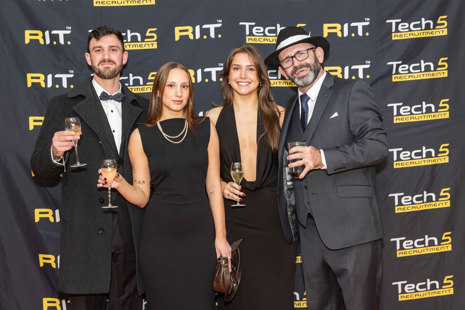 Four elegantly dressed professionals toast with champagne glasses at a Tech 5 RIT awards event.