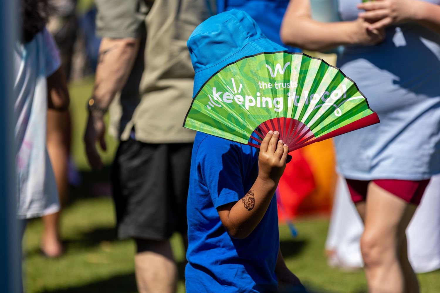 Crowd mingling at outdoor event with decorative green fan visible.