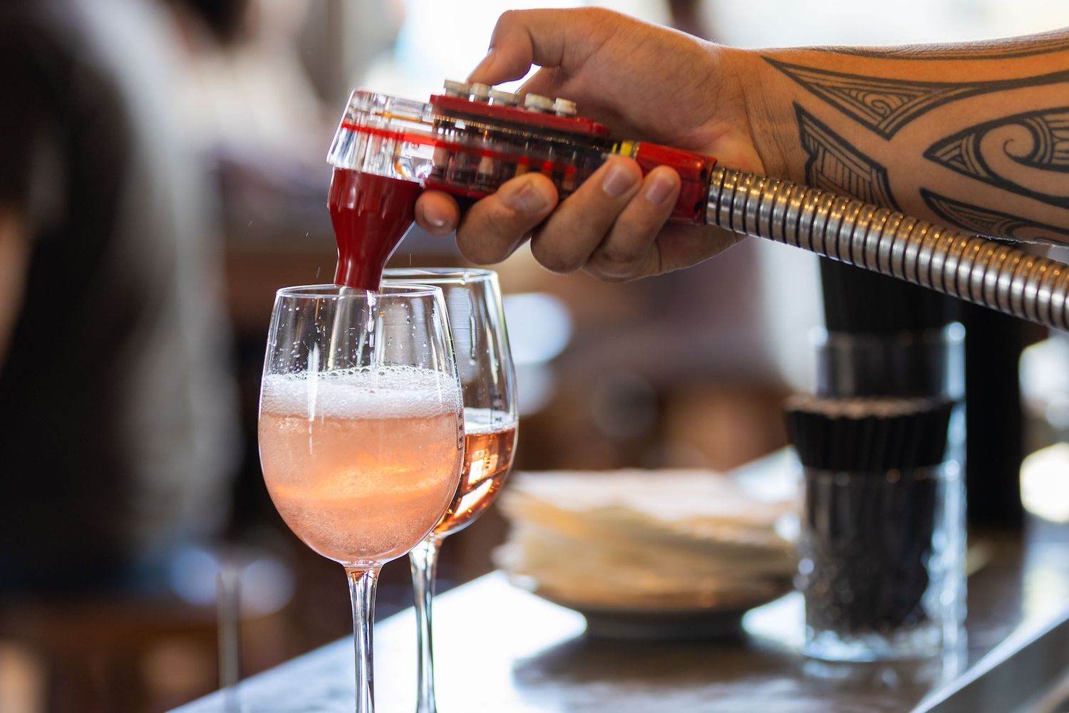 Hands pour pink cocktails from shakers into elegant stemmed glasses at a bar counter.