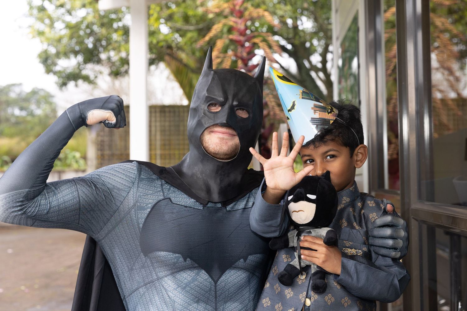 Child and adult dressed as Batman posing together outdoors at a costume event.