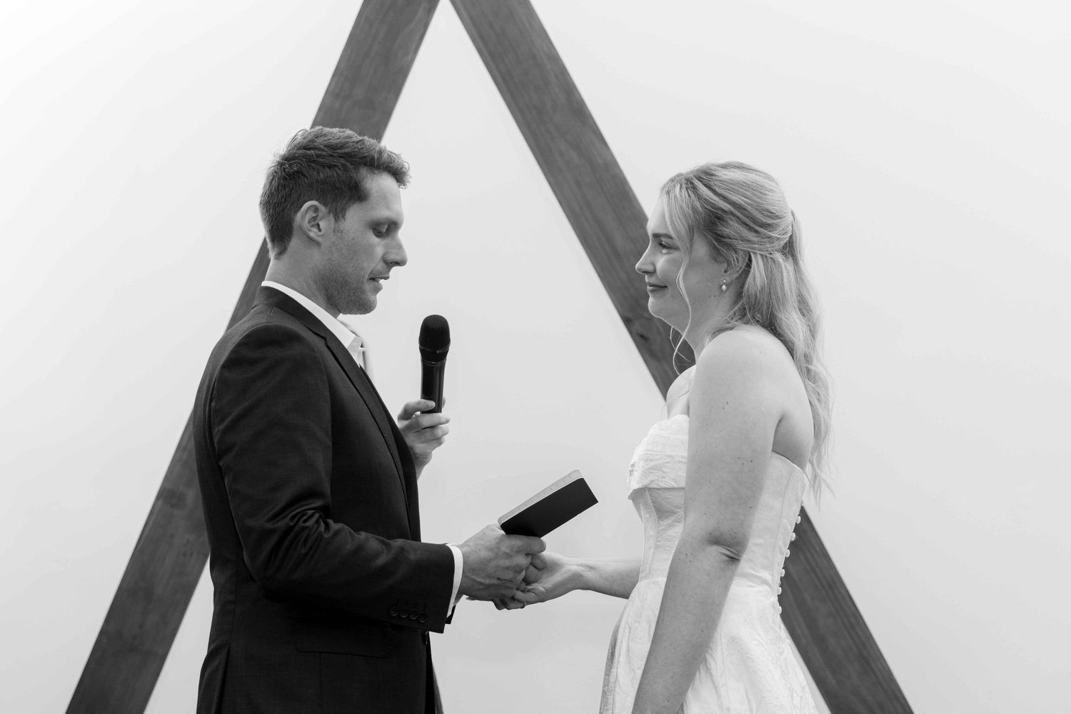 Wedding ceremony moments against white backdrop with wooden triangle arch.