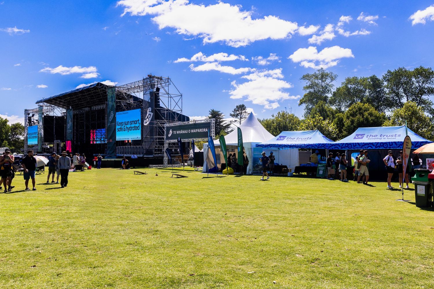 Large outdoor event setup with stage and promotional tents on green grass under blue sky.