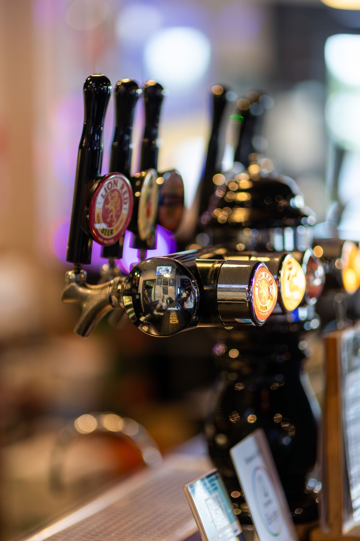 Close-up of beer taps in a row at a bar with blurred background lighting.