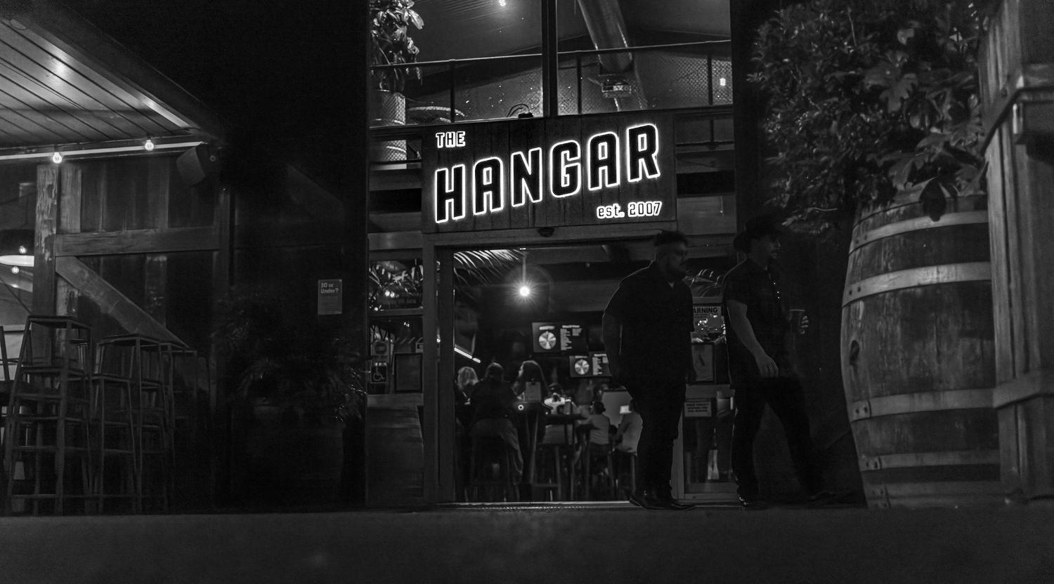 Dark moody urban street scene at night with neon signs and silhouettes of buildings in black and white.