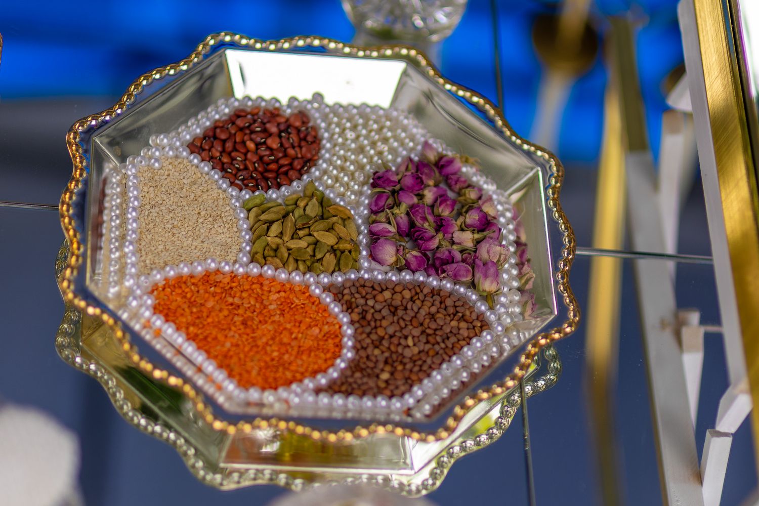 Decorative octagonal tray with pearls holding colorful spices, seeds, and dried flowers in elegant display.