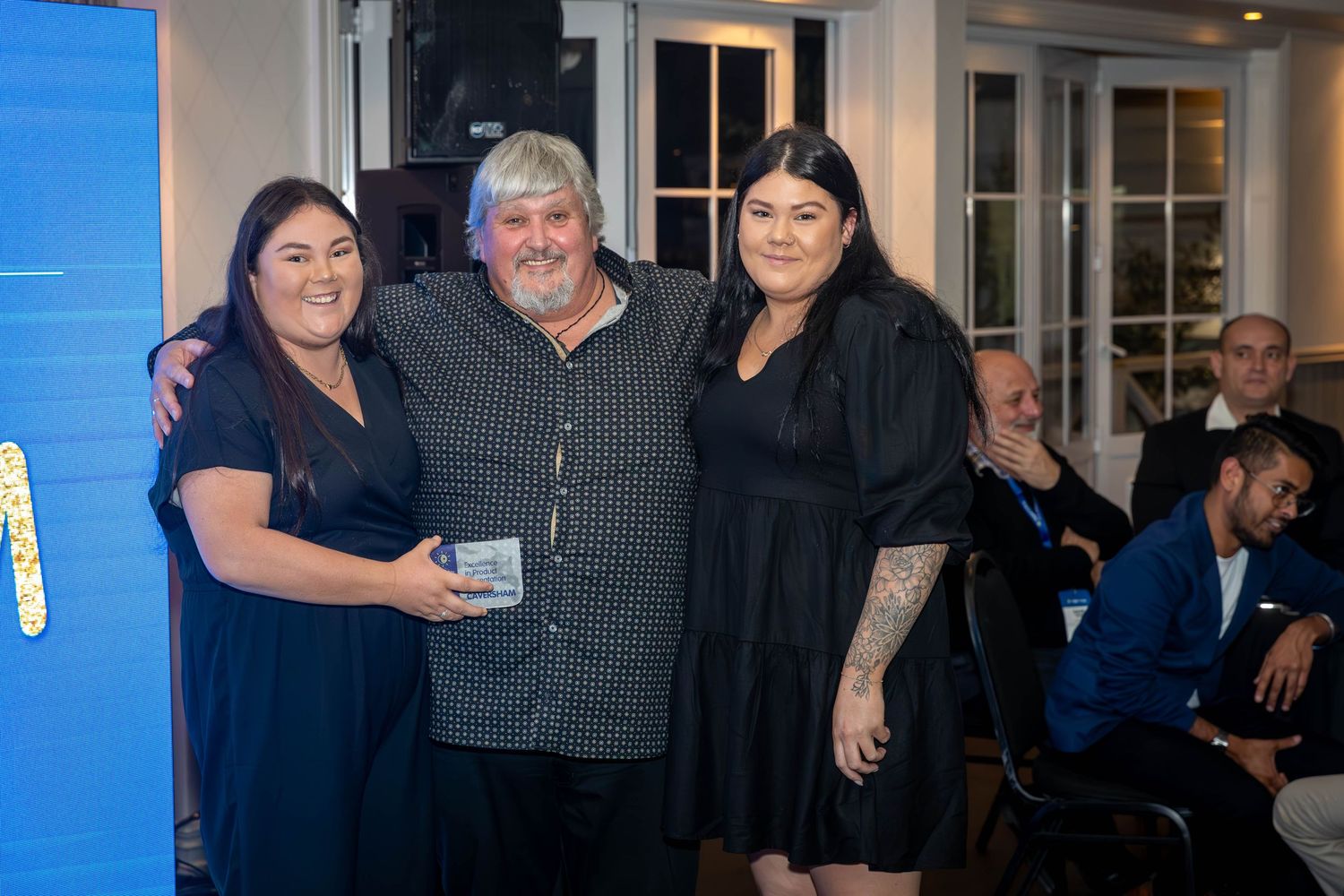 Three people smiling and posing together at a formal evening event in an elegant indoor venue.