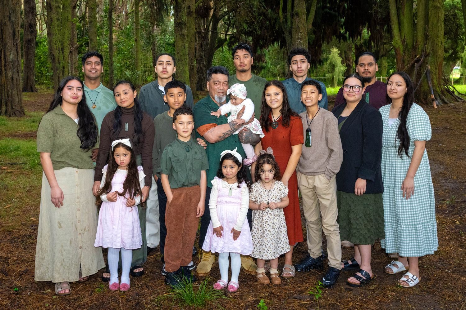 Large multigenerational Hispanic family posing together outdoors in a lush green forest park setting.