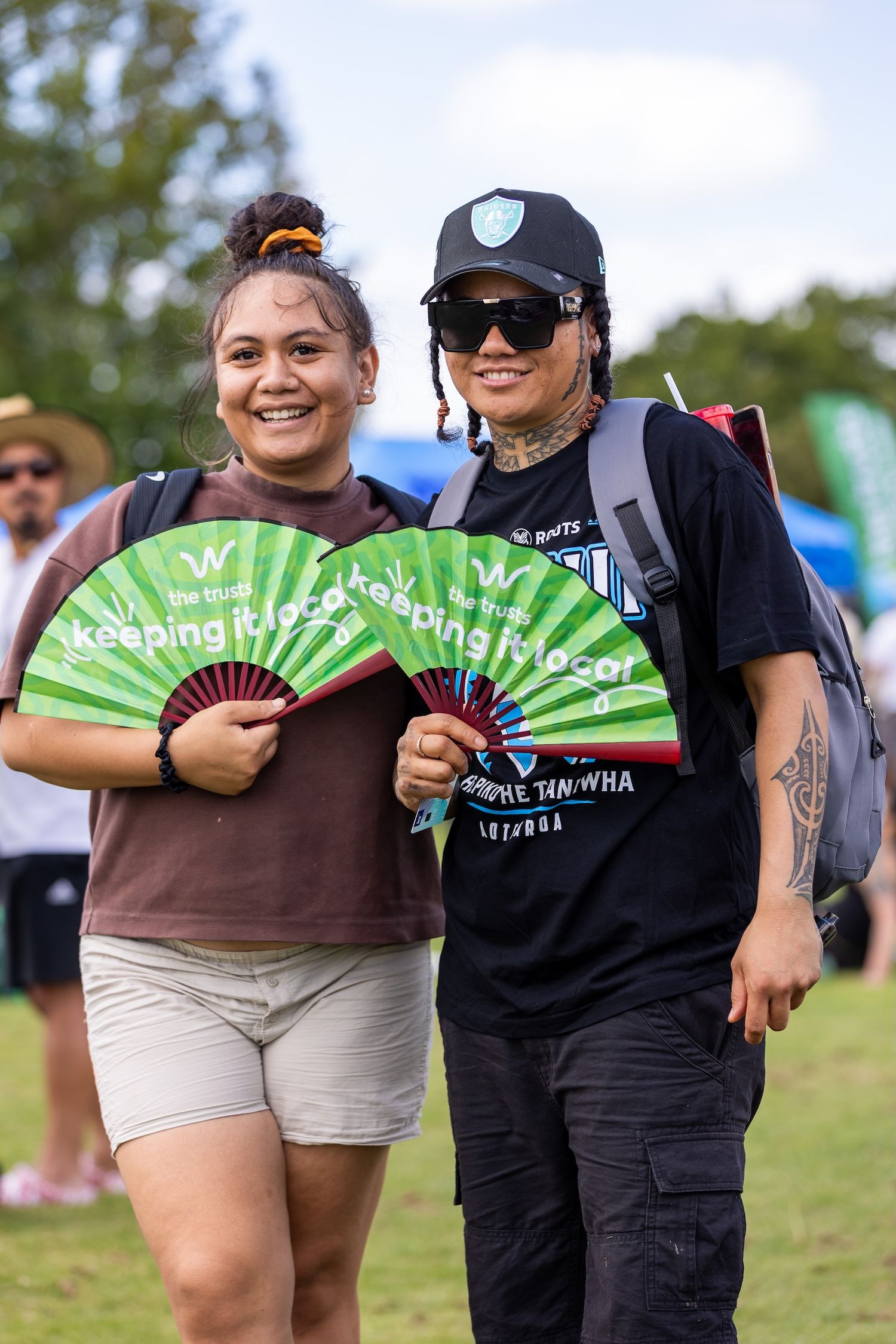 Group of friends posing with bright green promotional fans at outdoor festival.