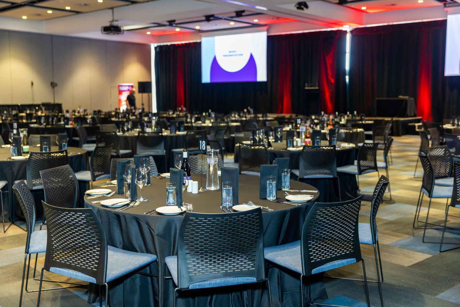 Corporate dining setup with round tables and chairs in a modern event space with ambient lighting.