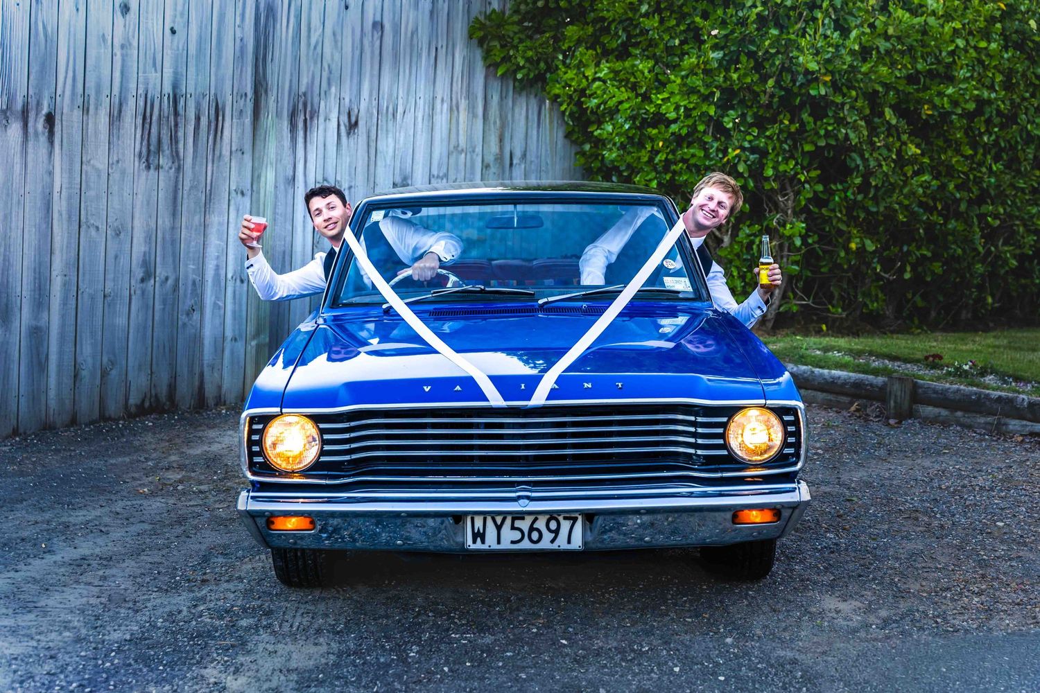 Couple celebrating in a blue vintage convertible car decorated with white ribbon bow for a wedding.