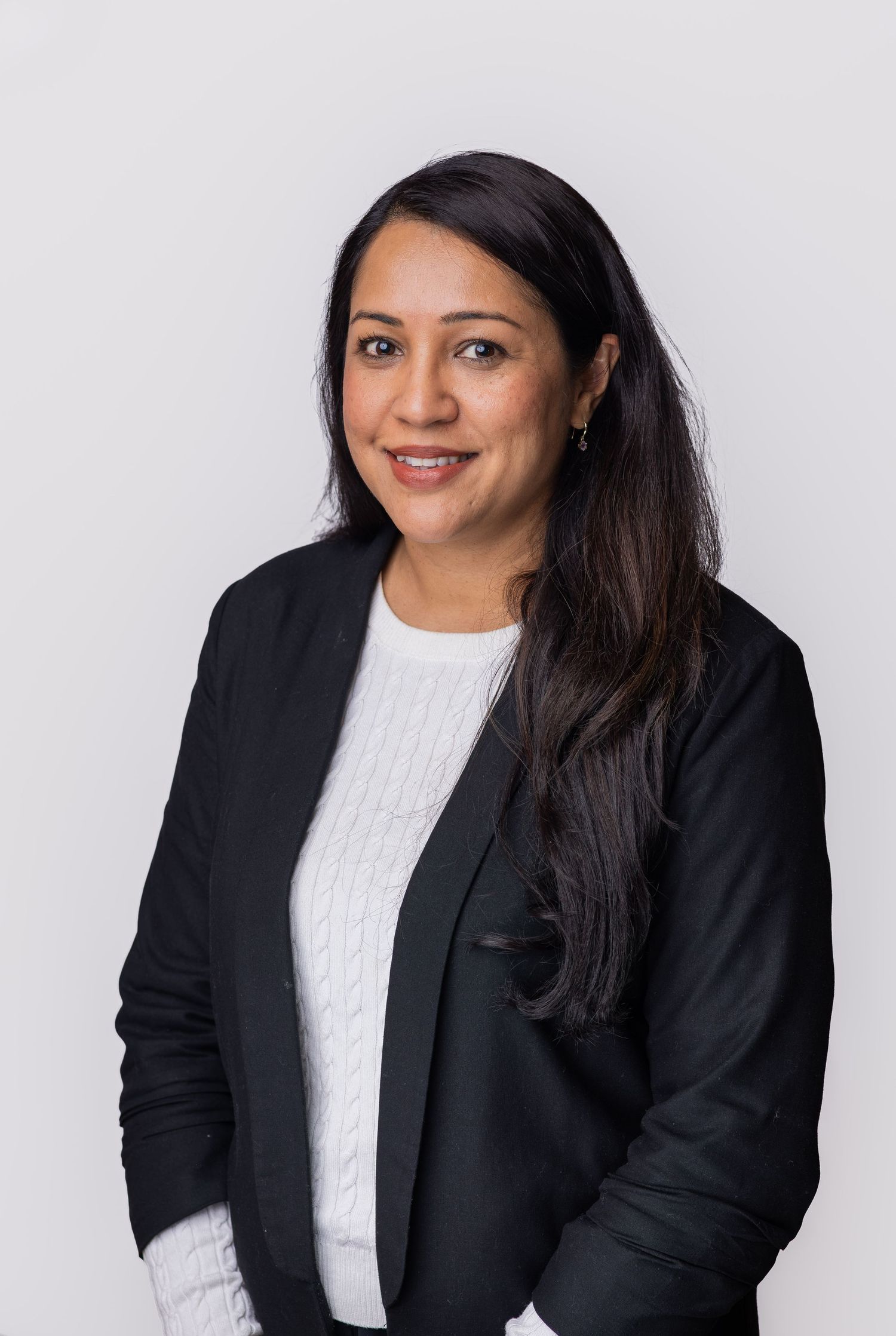 Professional woman in black blazer and white top smiling confidently against a light gray background.
