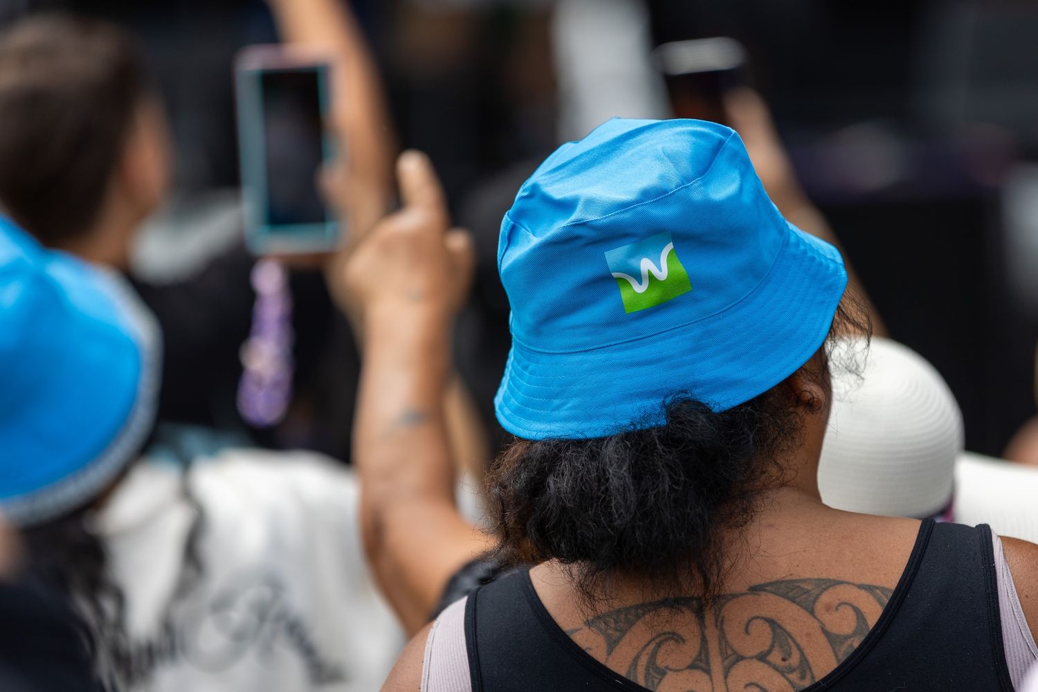 Crowd members with blue caps and tattoos at outdoor gathering.