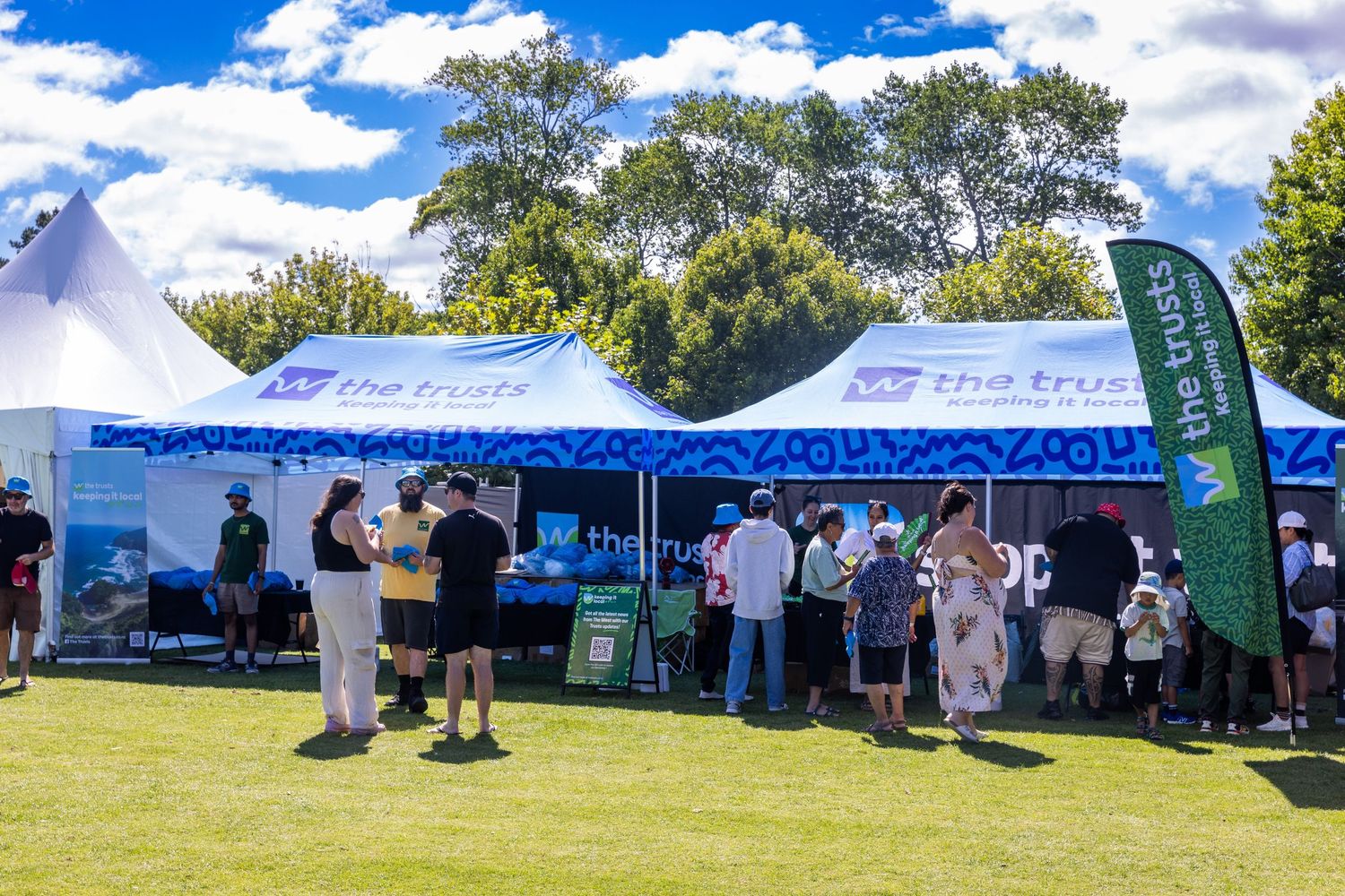 People gathering under blue and white branded tents at a sunny outdoor event.