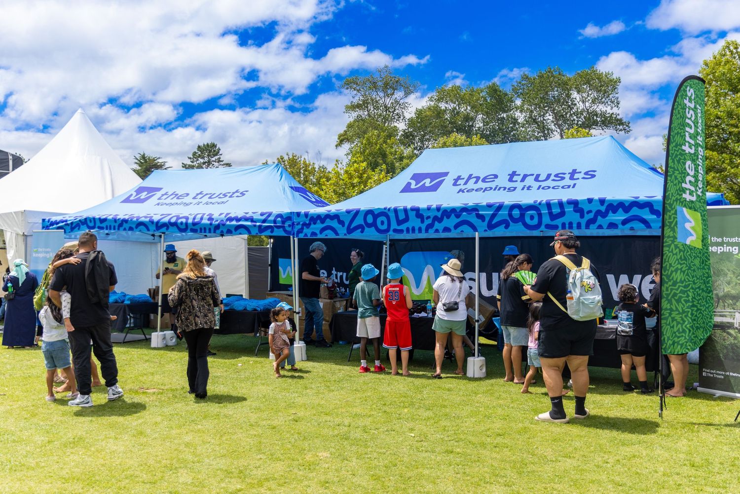Wide view of white event tents against blue sky with attendees gathering below.