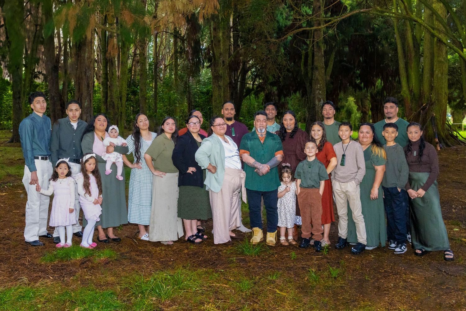 Large multigenerational family group portrait outdoors among tall green trees in a lush forest setting.