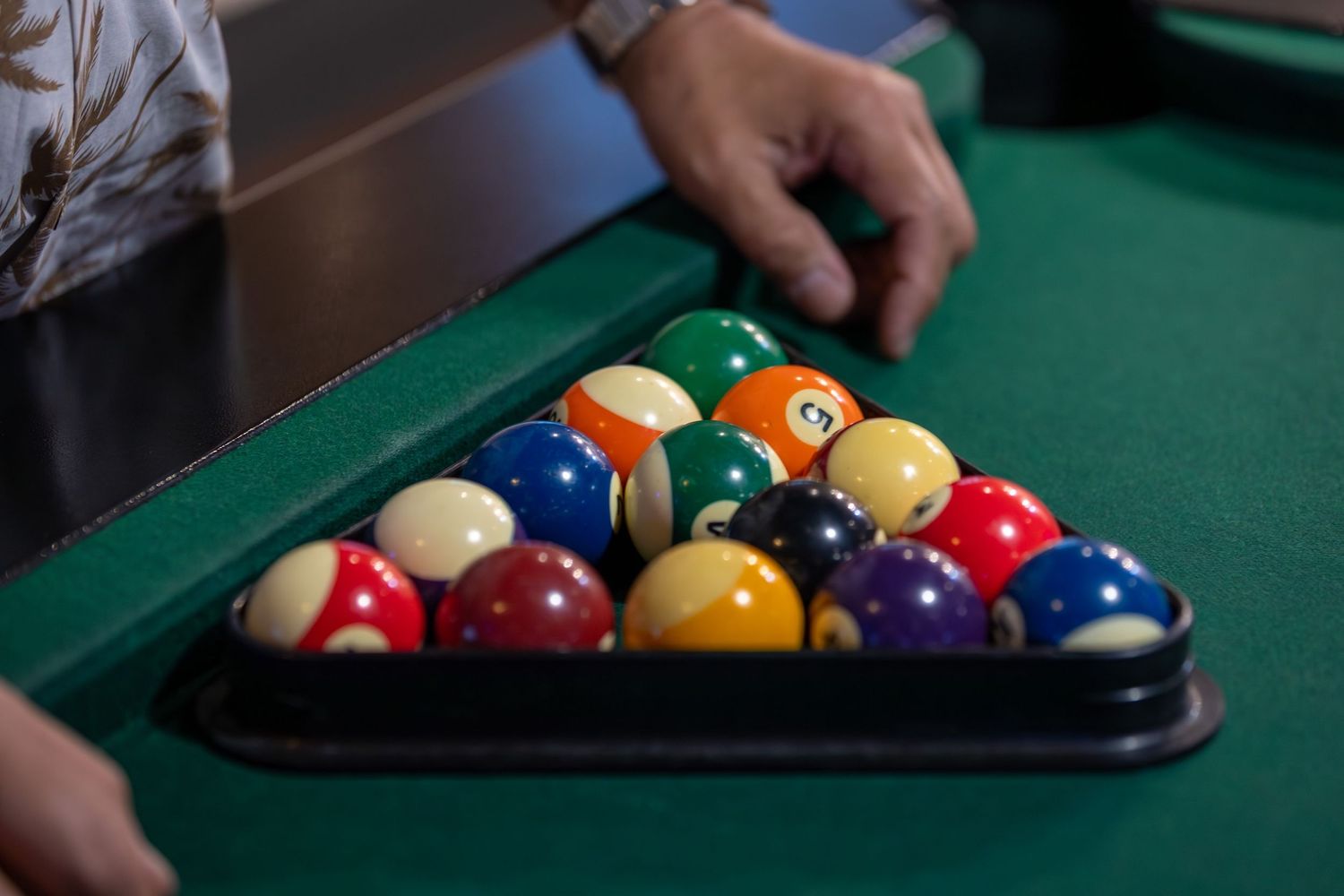 Setting up pool balls in triangle rack on green felt billiards table.