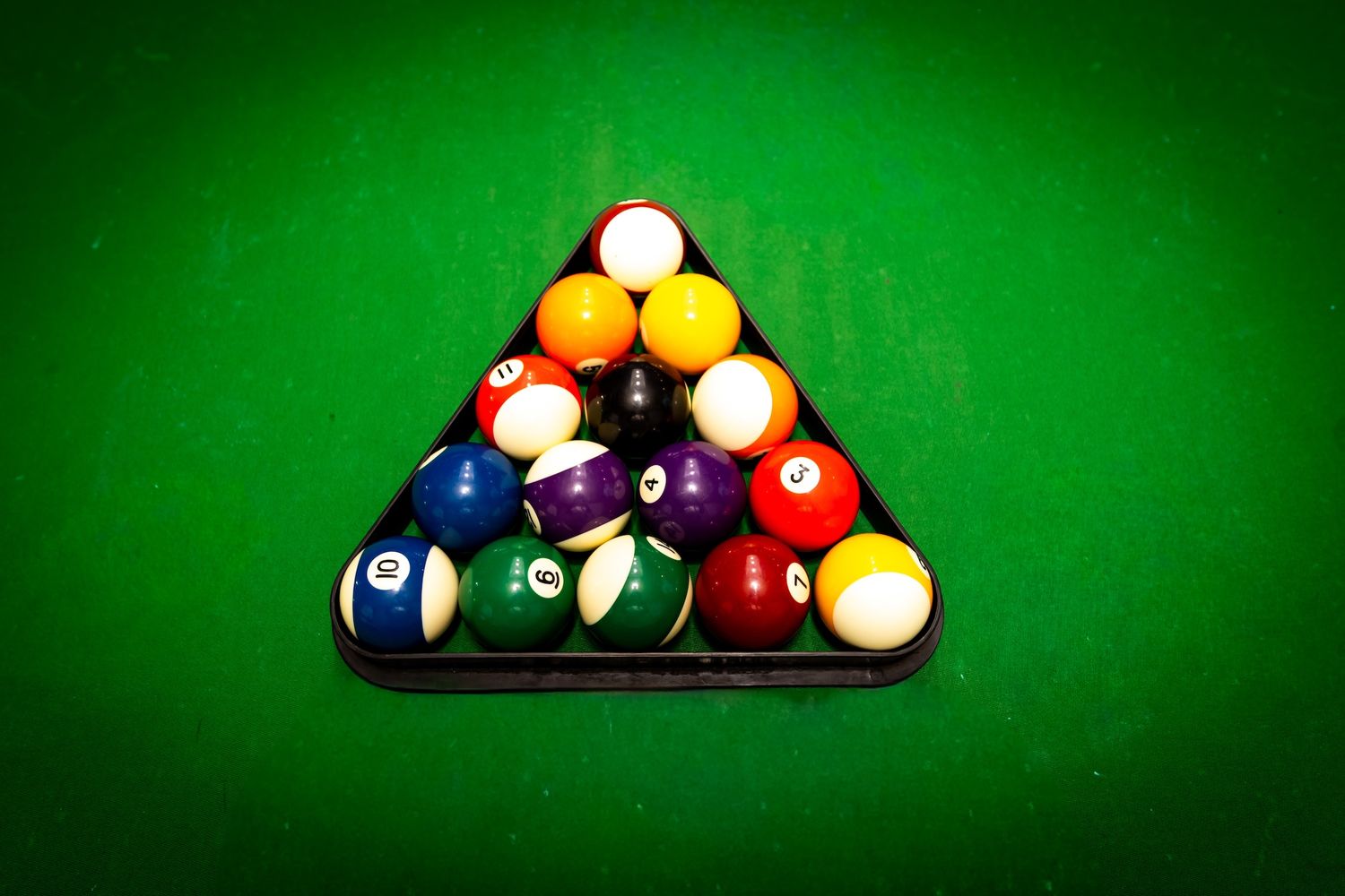 Pool balls arranged in a triangular rack formation on a green felt billiards table with dramatic lighting.