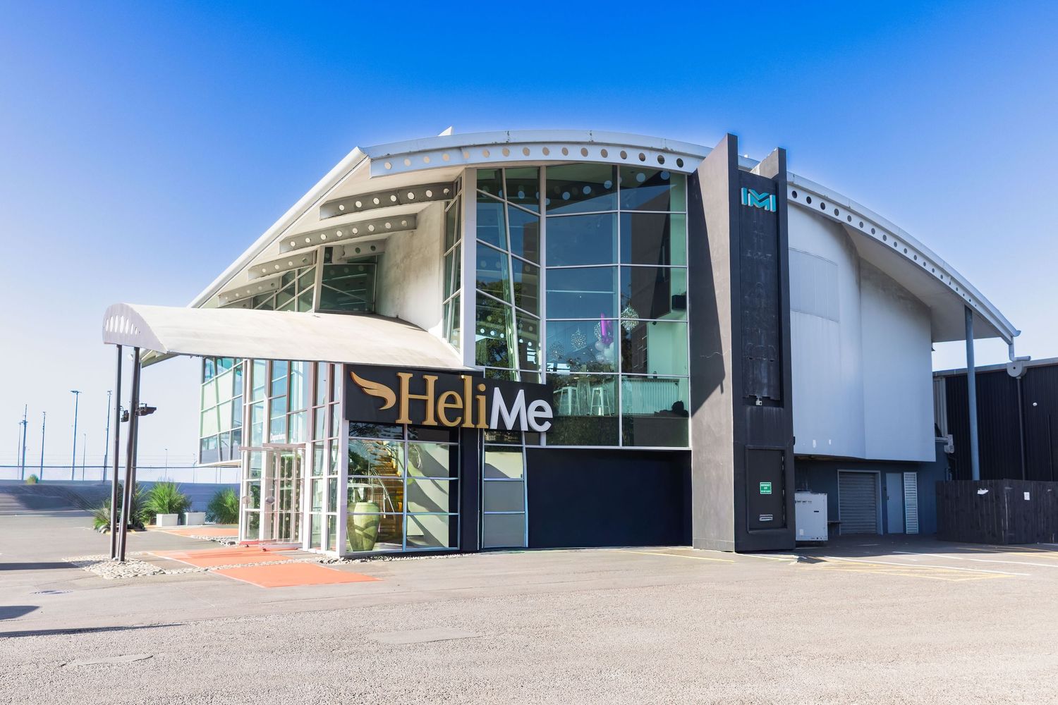 Exterior view of the modern HeliMe building with glass facade under a clear blue sky.