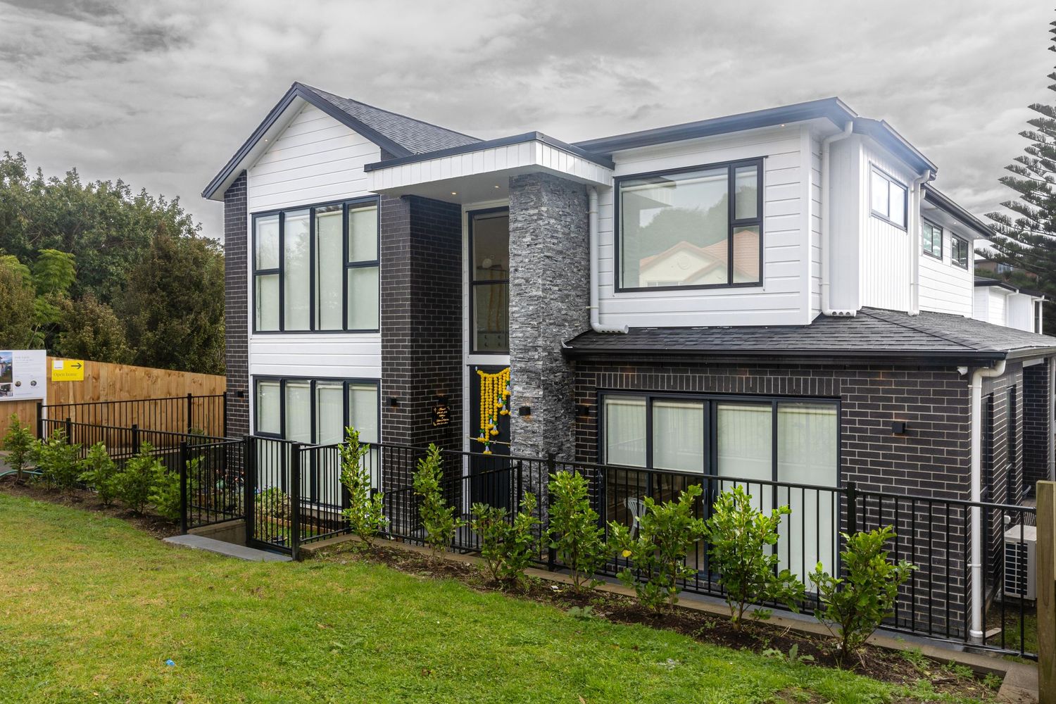 Modern two-story home with dark brick facade, white weatherboard upper level, large windows, and manicured lawn.