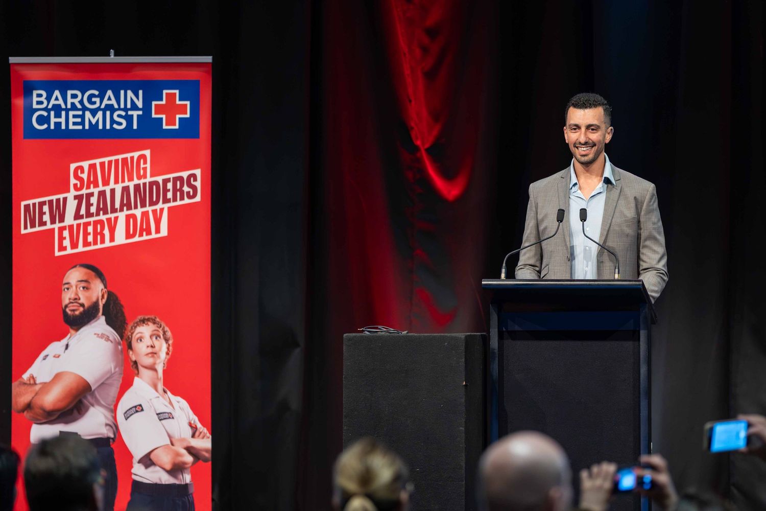 Corporate stage with Bargain Chemist branding and red accent lighting during presentation.