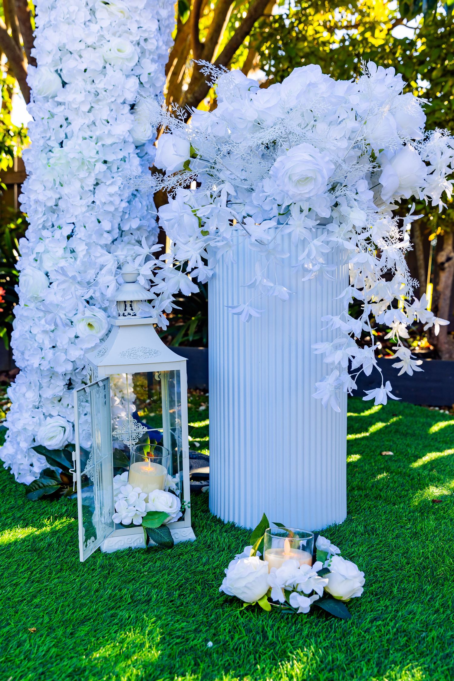 White floral arch with lantern and candles on green grass for elegant outdoor wedding ceremony decor.