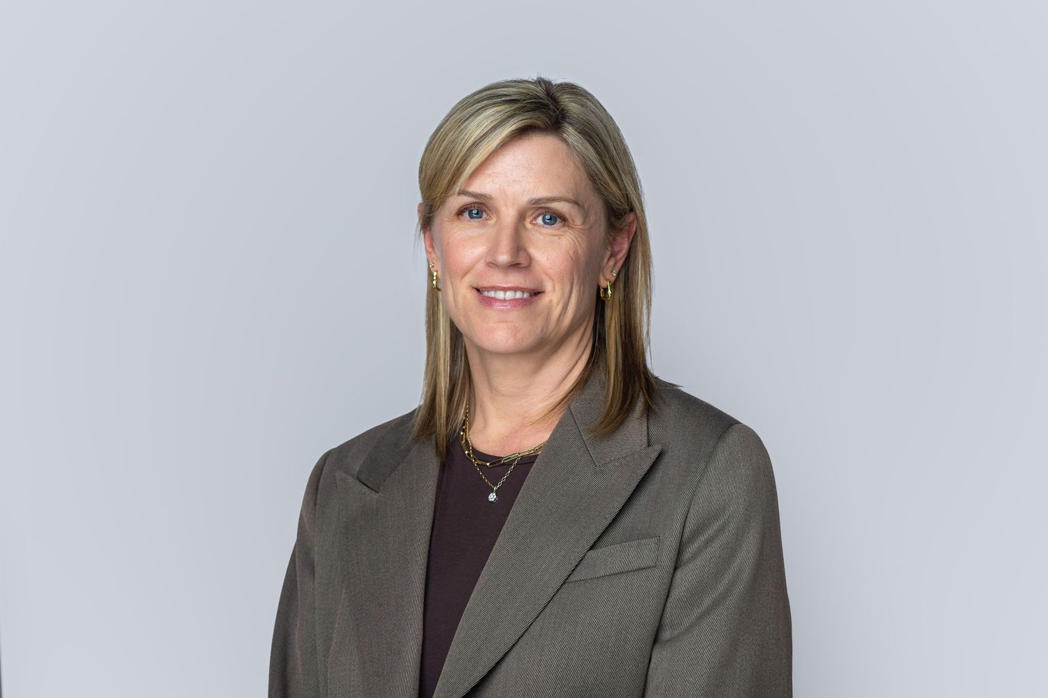 Professional headshot of a smiling businesswoman with blonde hair wearing a gray blazer against a light background.
