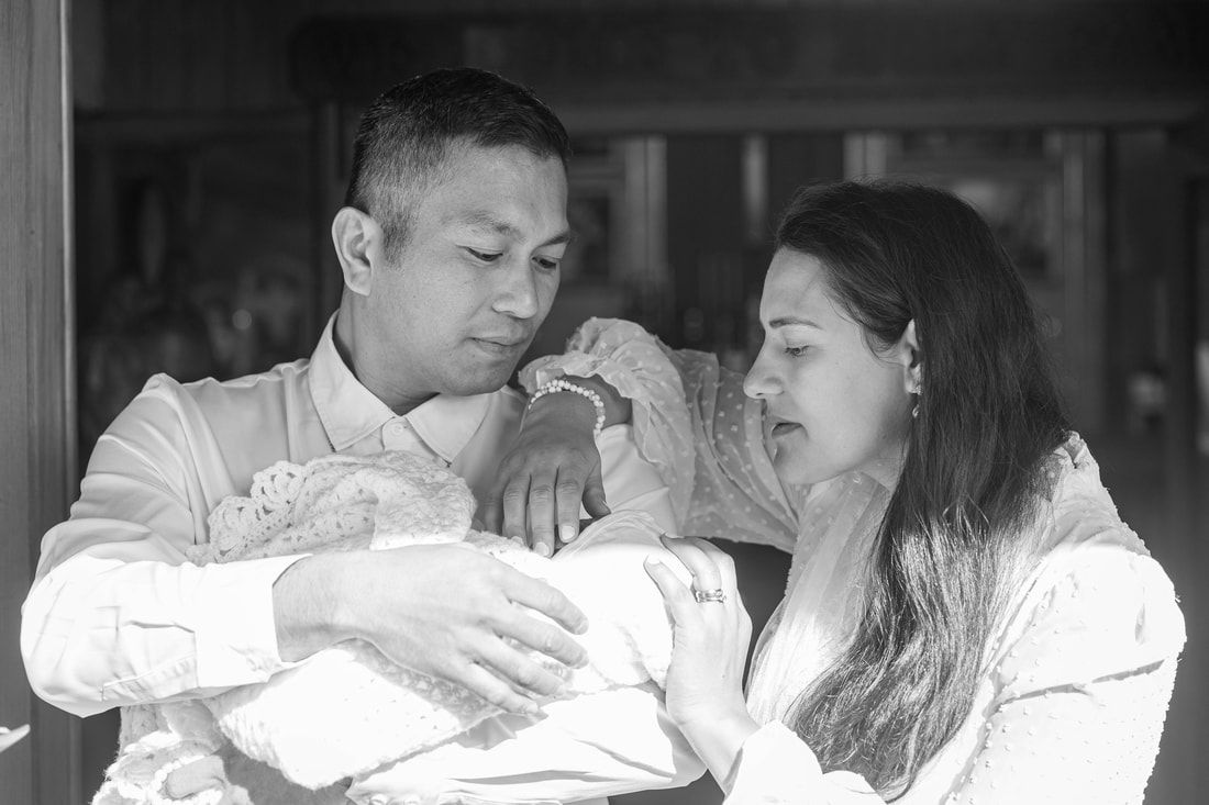 Black and white photo of a couple tenderly holding their newborn baby together.