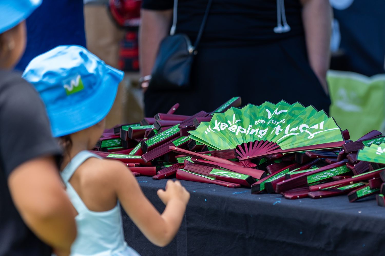 Collection of folding fans in green and burgundy colors displayed at outdoor event.