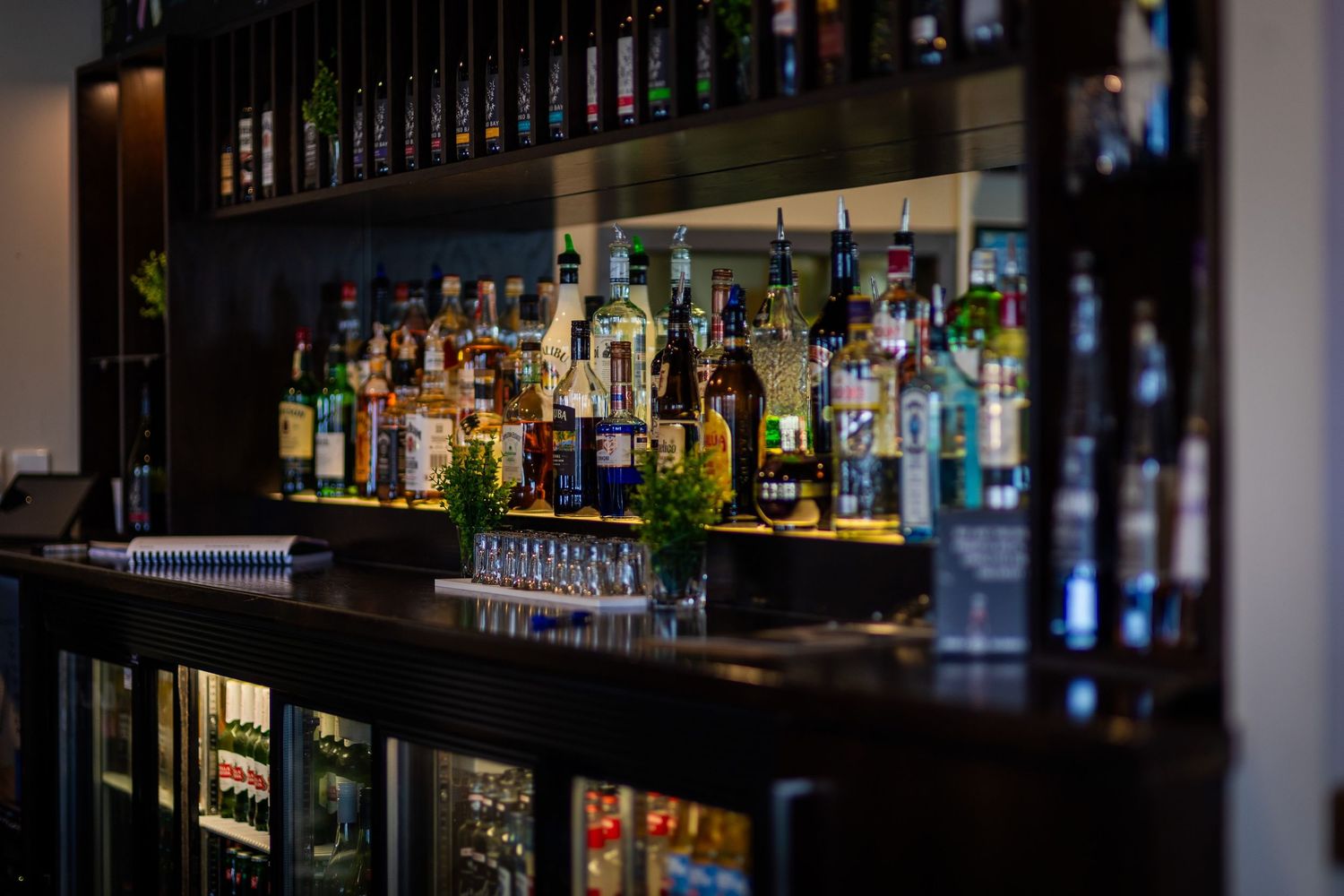 Dimly lit bar interior showing rows of premium spirits and liquor bottles on shelving.