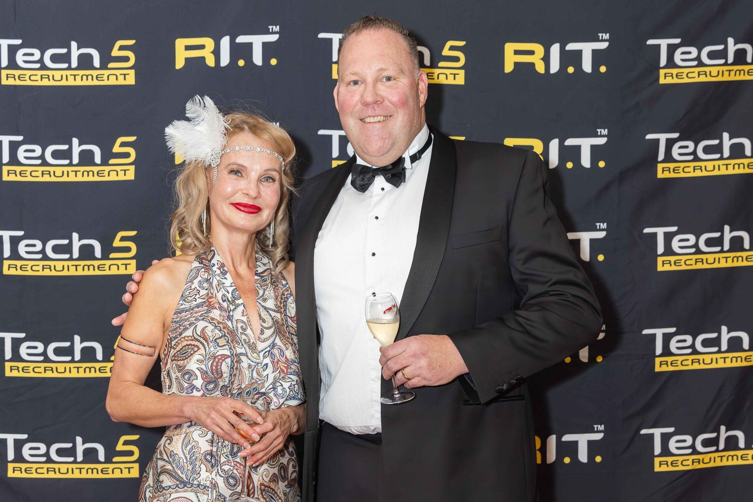A man and woman in formal attire pose together at a Tech5 Recruitment event backdrop.