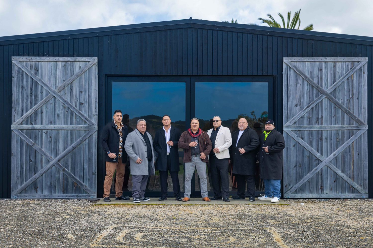 Group of eight people posing in front of a modern black barn-style building with large wooden doors.