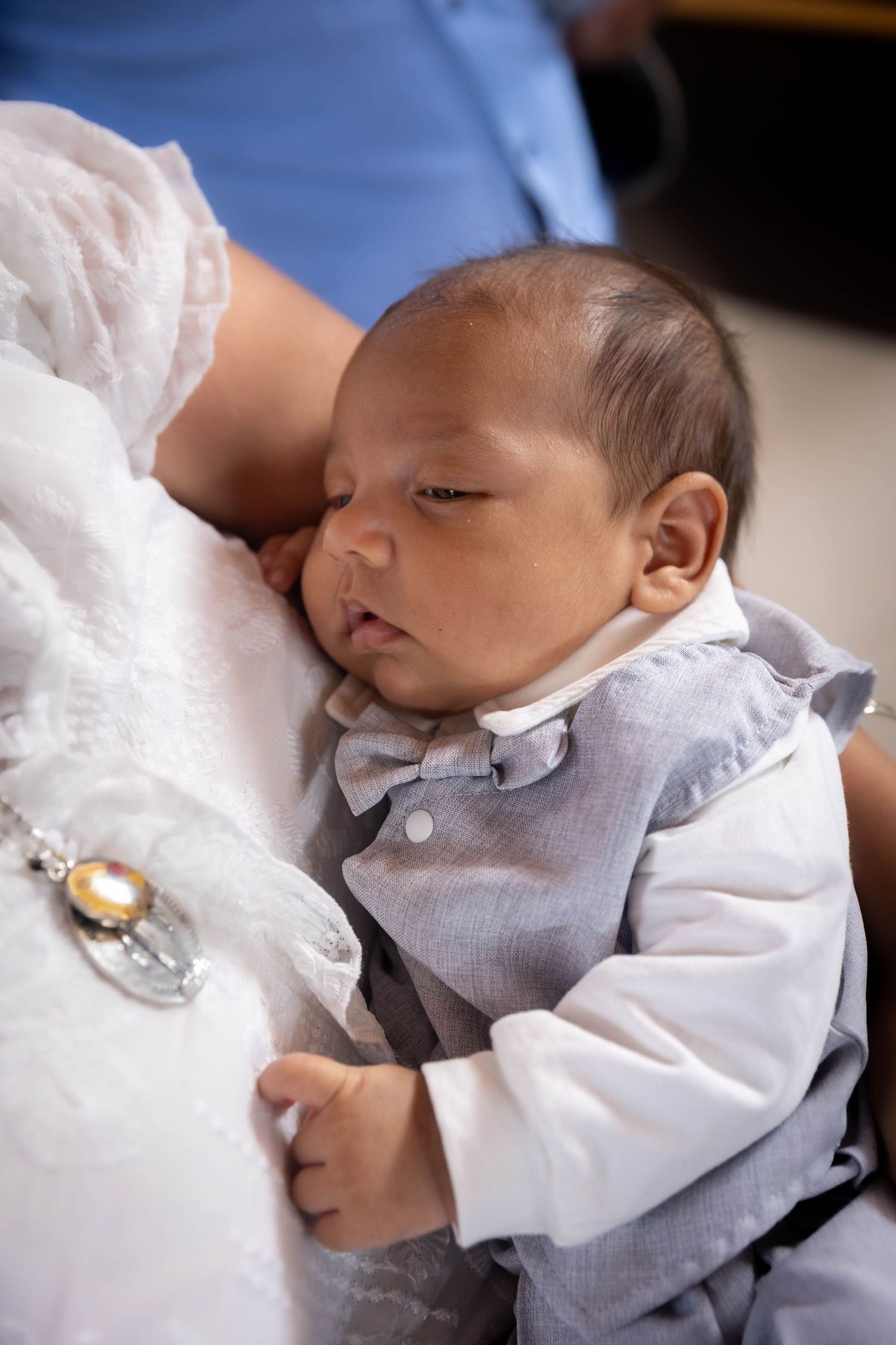 Newborn baby boy in gray bow tie suit sleeping peacefully in arms during a formal occasion.