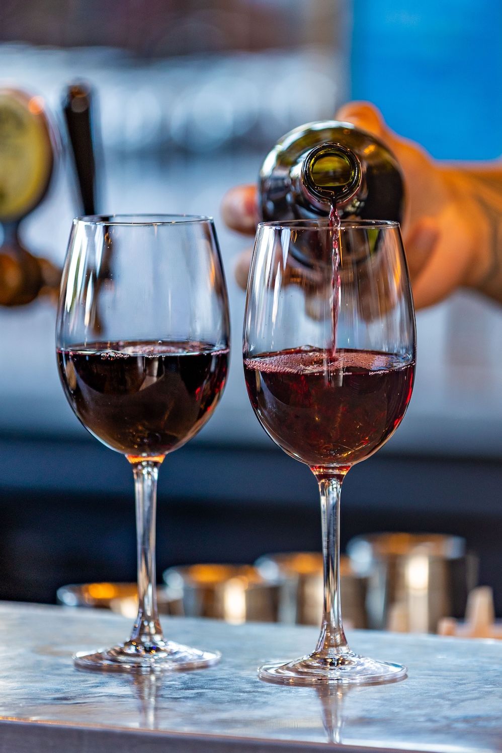 Red wine being poured into elegant stemmed glasses on a marble bar counter in sequence showing the pouring motion.